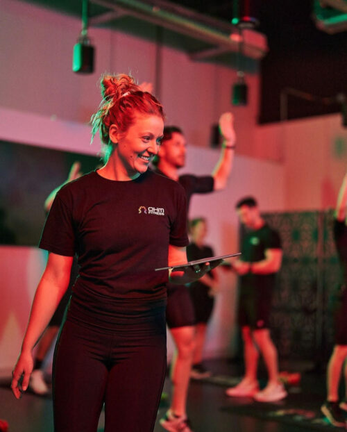 An instructor in an Ohm Fitness shirt leads the group through a workout using her handheld tablet.