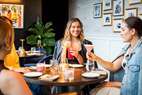 Group of women enjoying colorful cocktails at a stylish restaurant with modern decor and wall art