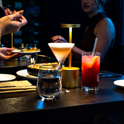 Cocktails, food, and people enjoying a dimly lit, upscale dining setting.