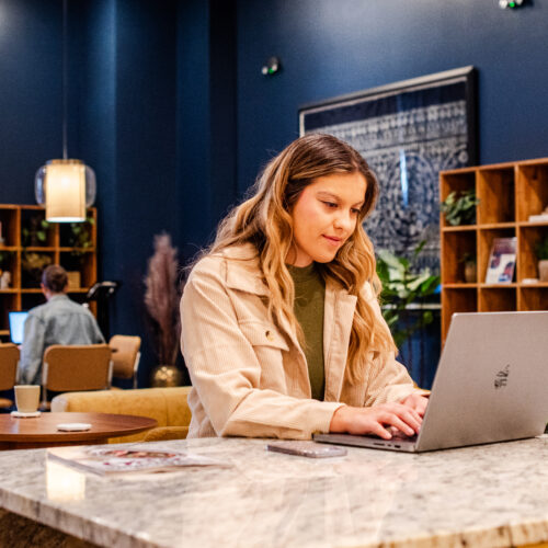 Woman working on a laptop in a cozy, modern coworking space with warm lighting and bookshelves.